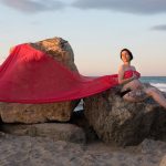 fotografía de embarazada en la playa del saler, Valencia, al atardecer. Tienen los ojos cerrados y lleva una tela roja.