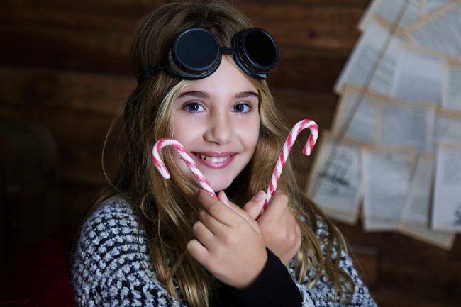 Niña divertida en sesión de fotos de Navidad con gafas steampunk y bastones de caramelo