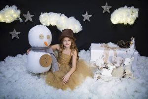 Niña en sesión de fotos de Navidad sobre nubes con muñeco de nieve y sombrero