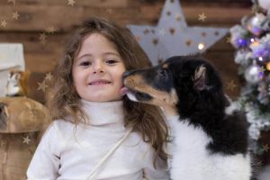 niña con su perrita sentada sobre nieve de algodón en sesión de Navidad