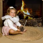 Niña observando la chimenea decorada con luces y calcetines navideños en una sesión de fotos en Valencia.