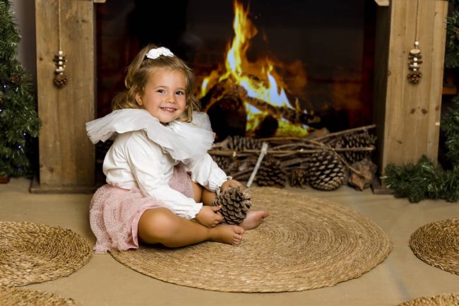 Niña frente a la chimenea decorada de Navidad Niña observando la chimenea decorada con luces y calcetines navideños en una sesión de fotos en Valencia.
