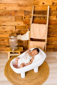 Bebé dormido en mini bañera con peluche blanco en sesión newborn