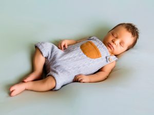 Bebé dormido con peto gris de punto durante sesión newborn profesional