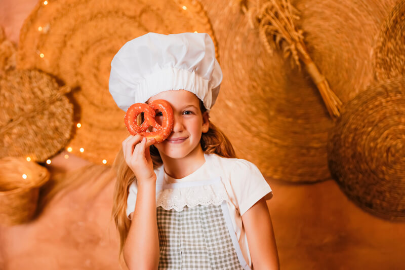 Sesión fotos Navidad Valencia – Niña divertida con pretzel sesión fotos Navidad Valencia niña con gorro de chef y pretzel