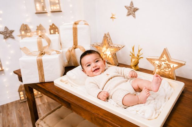 Bebé sonriente junto a regalos y estrellas de Navidad iluminadas