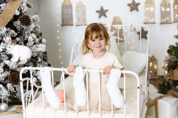 Niña pequeña sonriendo en una cama durante una sesión de fotos de Navidad en Valencia