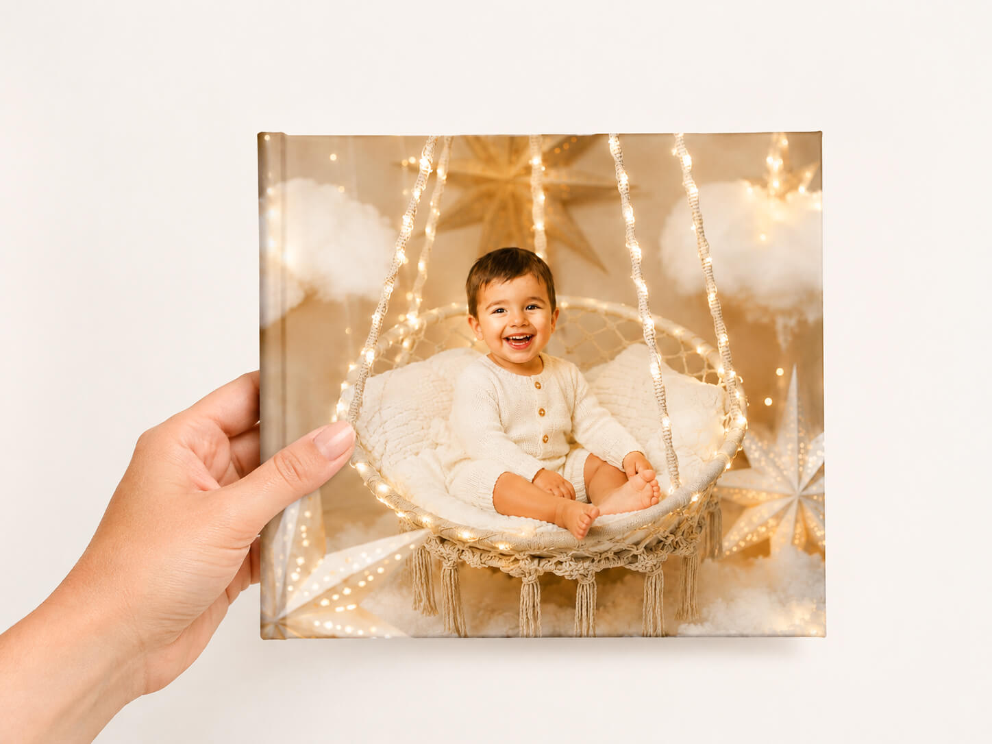 Mano sosteniendo el álbum impreso del Pack Premium de la sesión de fotos de Navidad en Valencia, con portada de un bebé en el escenario del Reino de las Nubes.